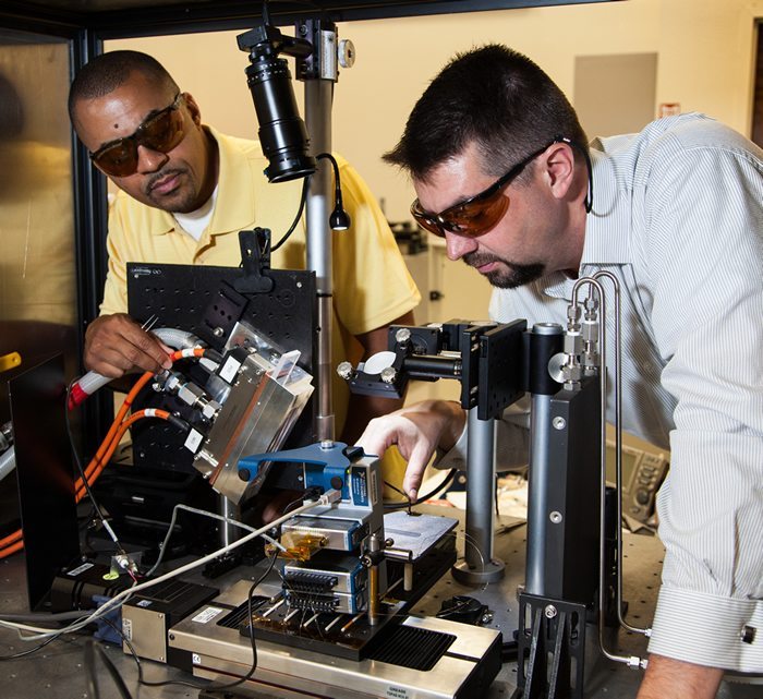 Ibo Matthews (left) adjusting a 4 KW laser. Image via.