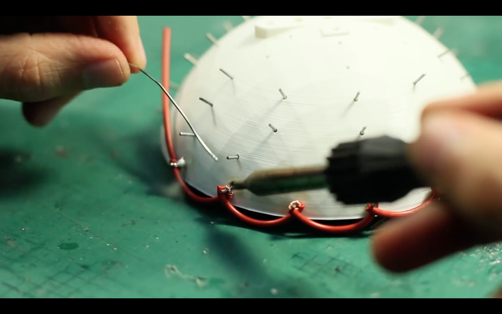 Soldering wires onto pins in the 3D printed cup. Screenshot via: BristolIG on Youtube