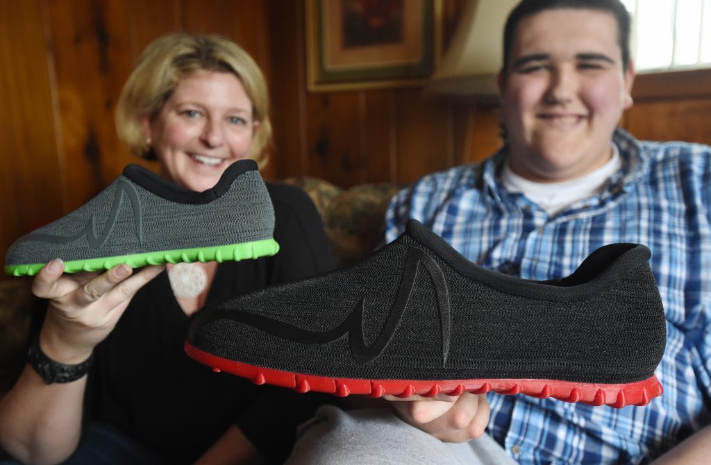 Bric Brown (right) holds one of his custom 3D printed Feetz shoes next to an average sized Feetz on the left. Photo via Jackson Citizen Patriot