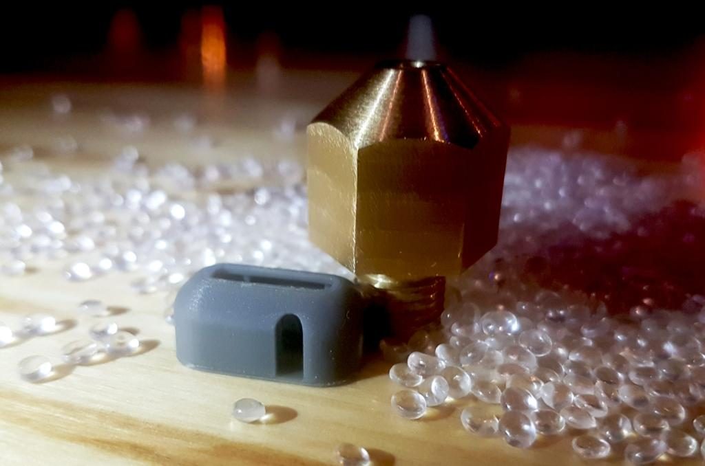 A miniature model of the Wave 3D printed camper beside a nozzle and pelletized feedstock. Photo via Create Café