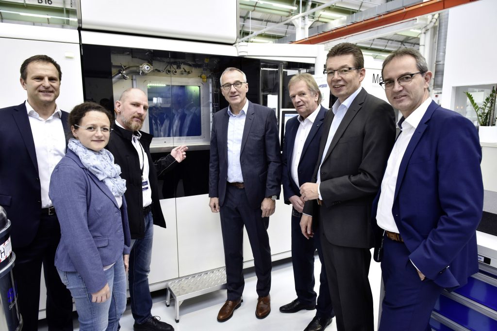 Oliver Pohl, Head of Additive Manufacturing at Volkswagen (third from left) presents the new 3D printing center to visitors from the European Works Council and management. To note: The machine in the background appears to be a MetalFAB1 system from Dutch manufacturer Additive Industries. Photo via Volkswagen