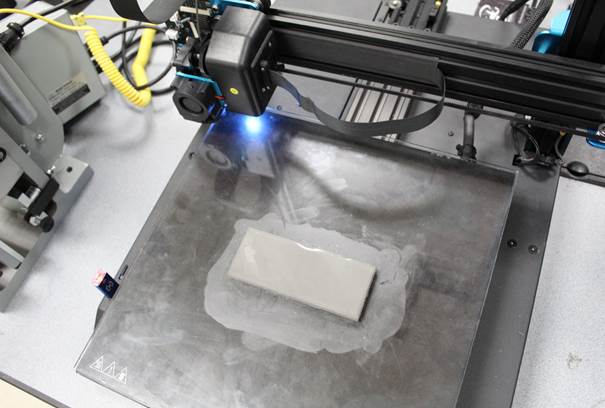 Modified low cost desktop 3D printer producing infused stainless steel plate. Photo via SCC.