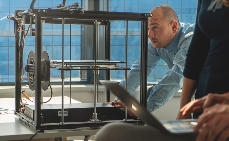 An engineer calibrating a 3D printer. Photo via NADDCON. 