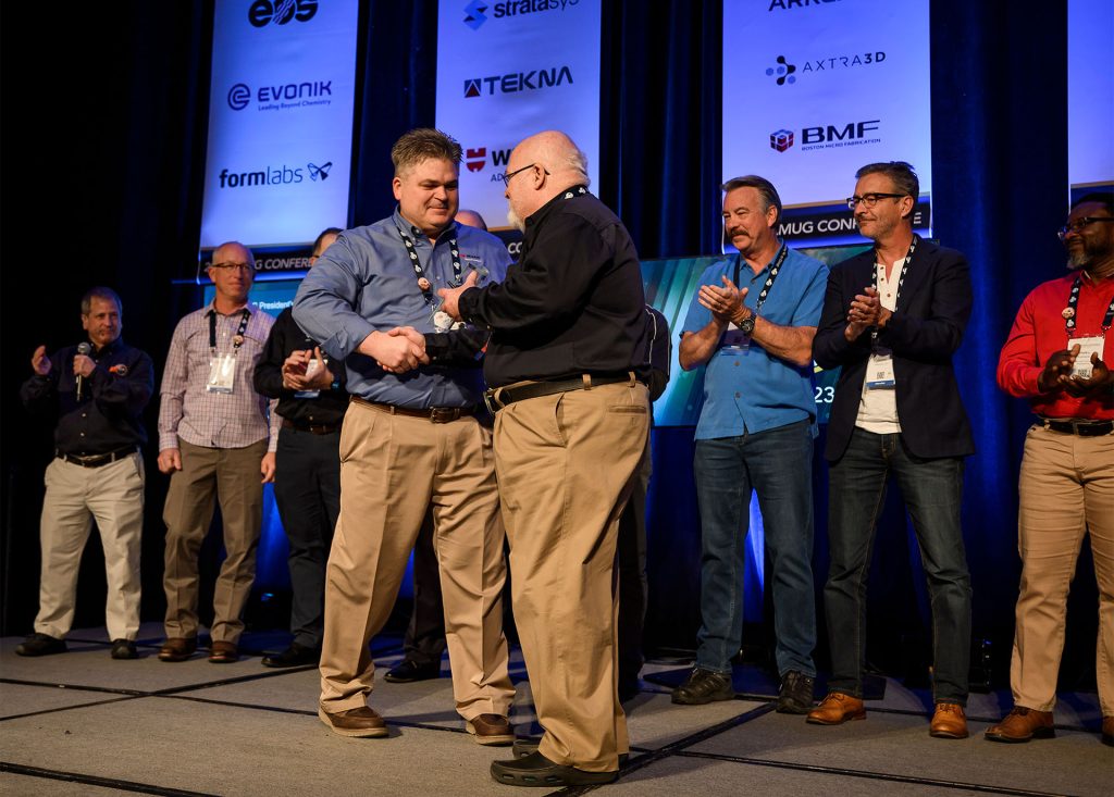 Mark Wynn (front left) receives the President’s Award from Mark Abshire, AMUG President. In honor of Wynn, past AMUG presidents gathered on the stage. Photo via AMUG.