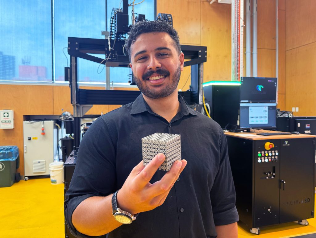 Jordan Noronha holding a sample of the new titanium lattice structure 3D printed in cube form. Photo via RMIT.