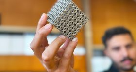 PhD candidate Jordan Noronha holding a sample of the new titanium lattice structure 3D printed in cube form. Photo via RMIT.