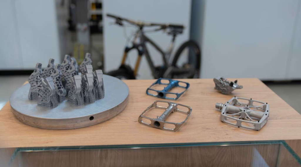 Left to right: Brake caliper for hydraulic mountain bike brakes, Titanium mountain bike pedal body, barrel finish and anodized, Aluminum bike pedal with bolted grip pins. Photo via TRUMPF.
