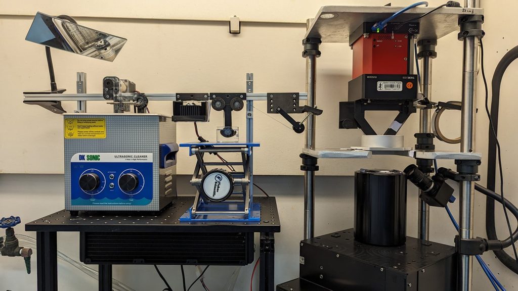 The r2rCLIP setup in the DeSimone lab runs from right to left. The printing occurs at the area below the red piece. Photo via DeSimone Research Group.