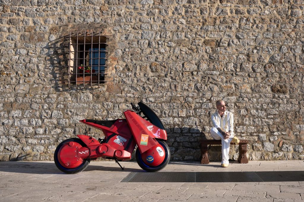 J Balvin sits on a bench beside the 3D printed Akira-inspired electric motorcycle. Photo via DAB Motors / Vita Veloce Team.