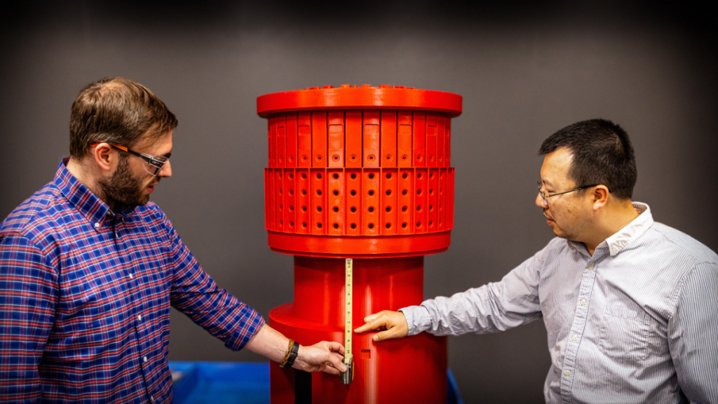 Samuel Sheckman, a mechanical engineer, left, and Danny Cai, a senior engineer, with the 3D model of the top of the toroidal field coil. Photo via PPPL.